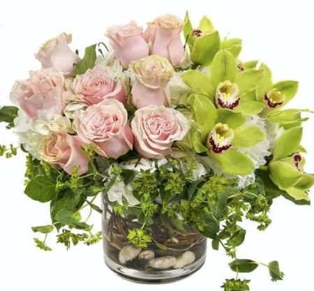 Luxurious blooms in lime green, pink and white hues. Large cymbidium orchids are surrounded by premium hydrangea and roses, all gathered tightly within a cylindrical vase reflecting the beauty of English garden that has been enjoyed for centuries. Exact greenery may vary.