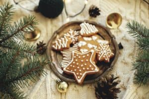 Christmas gingerbread cookies on plate, fir branches, ornaments and warm lights on cozy knitted background. Atmospheric winter time and hygge home. Merry Christmas and Happy Holidays